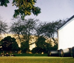 People watching an outdoor pop-up cinema screen in a park at dusk