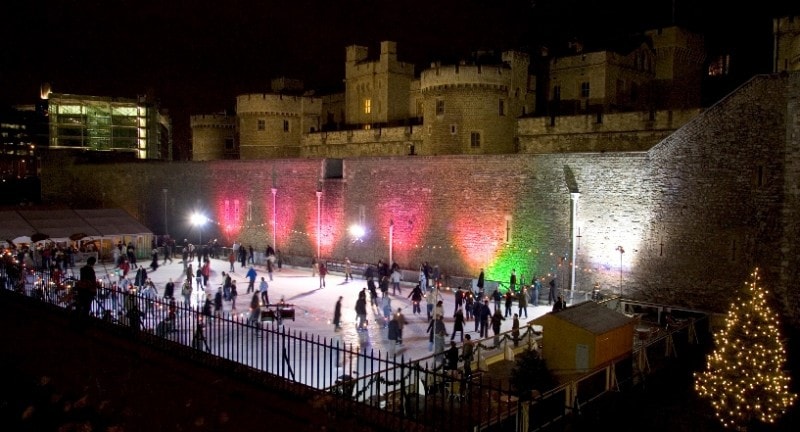 people ice skating after dark at the tower of london