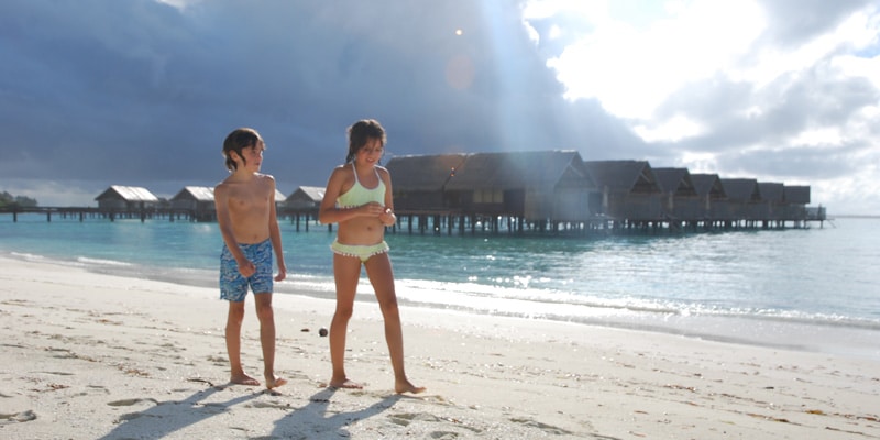 two-children-on-white-sand-beach-in-the-Maldives-with-overwater-villas-behind
