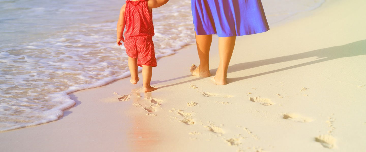 mother and daughter walking on sandy beach