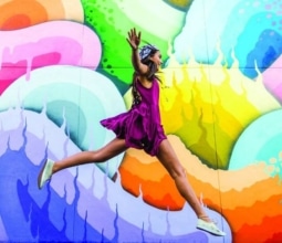 girl jumping in front of colourful painted wall